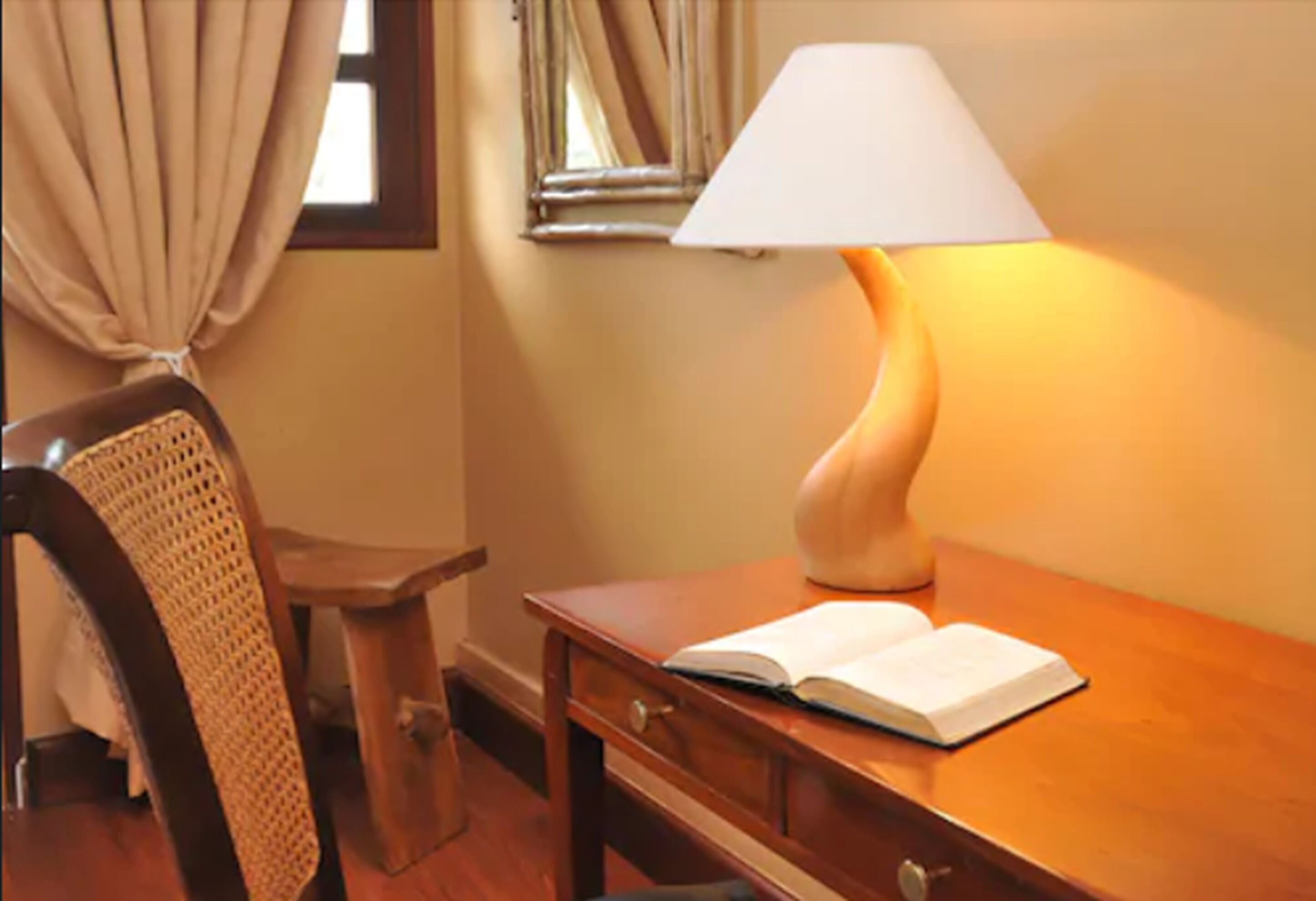 A wooden desk with an open book, a lamp, and a chair with a woven backrest.