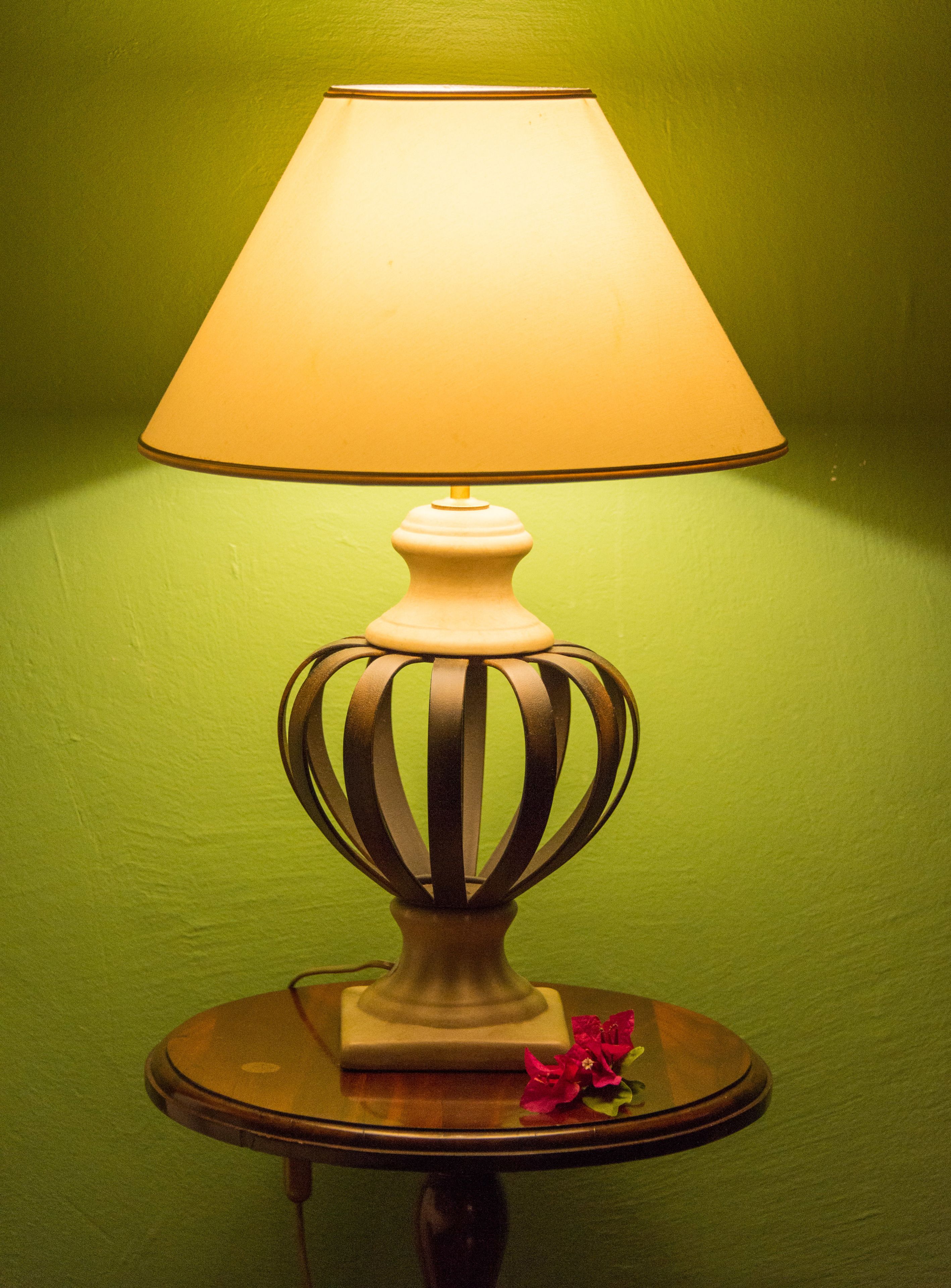 A table lamp with a white shade and a decorative base, placed on a round table with a green wall in the background.