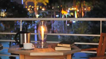 A table with a candle, a book, and a cup on a balcony overlooking a cityscape at night.