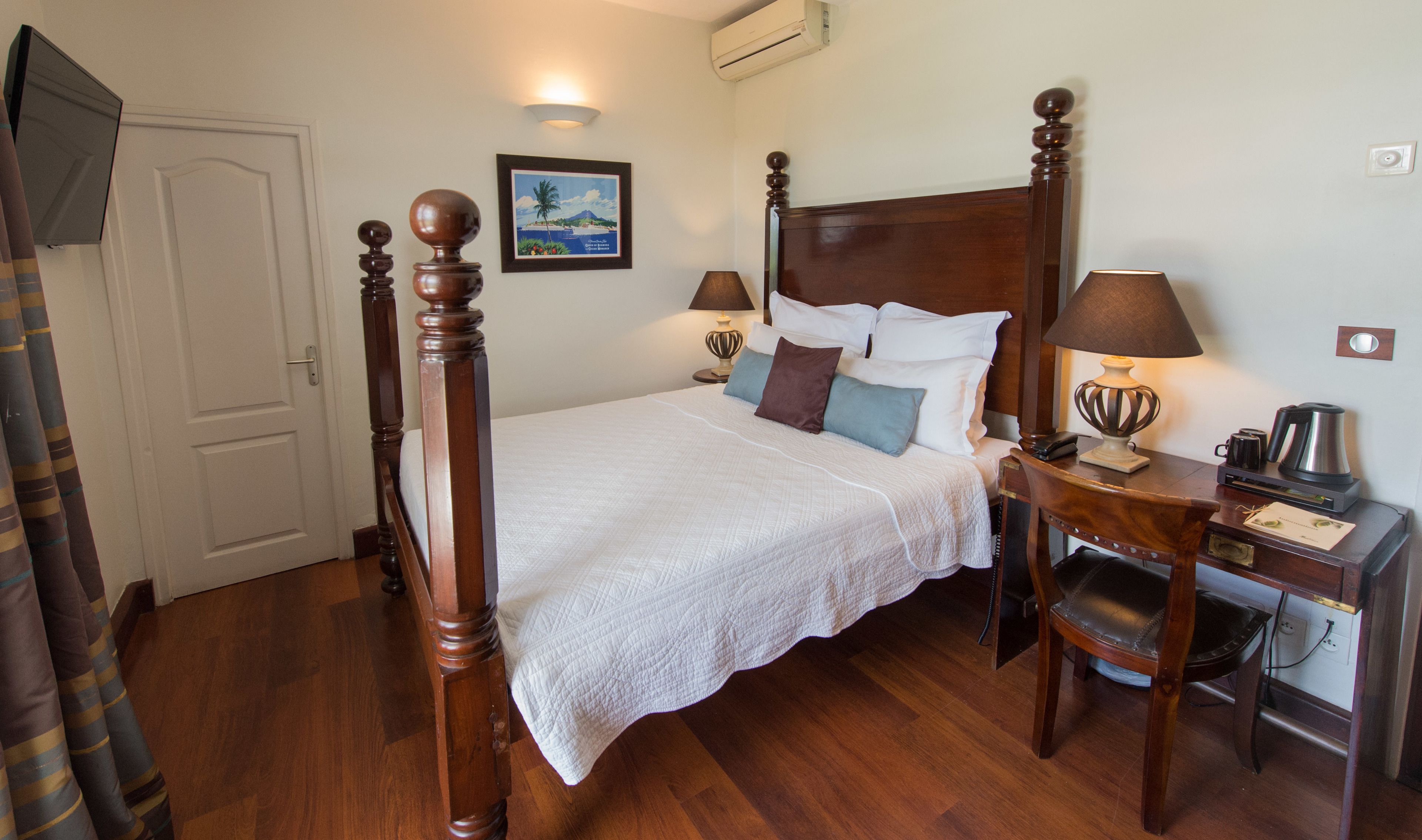 Una cama bien hecha con cabecera de madera, una mesita de noche con lámpara y un cuadro enmarcado en la pared.
