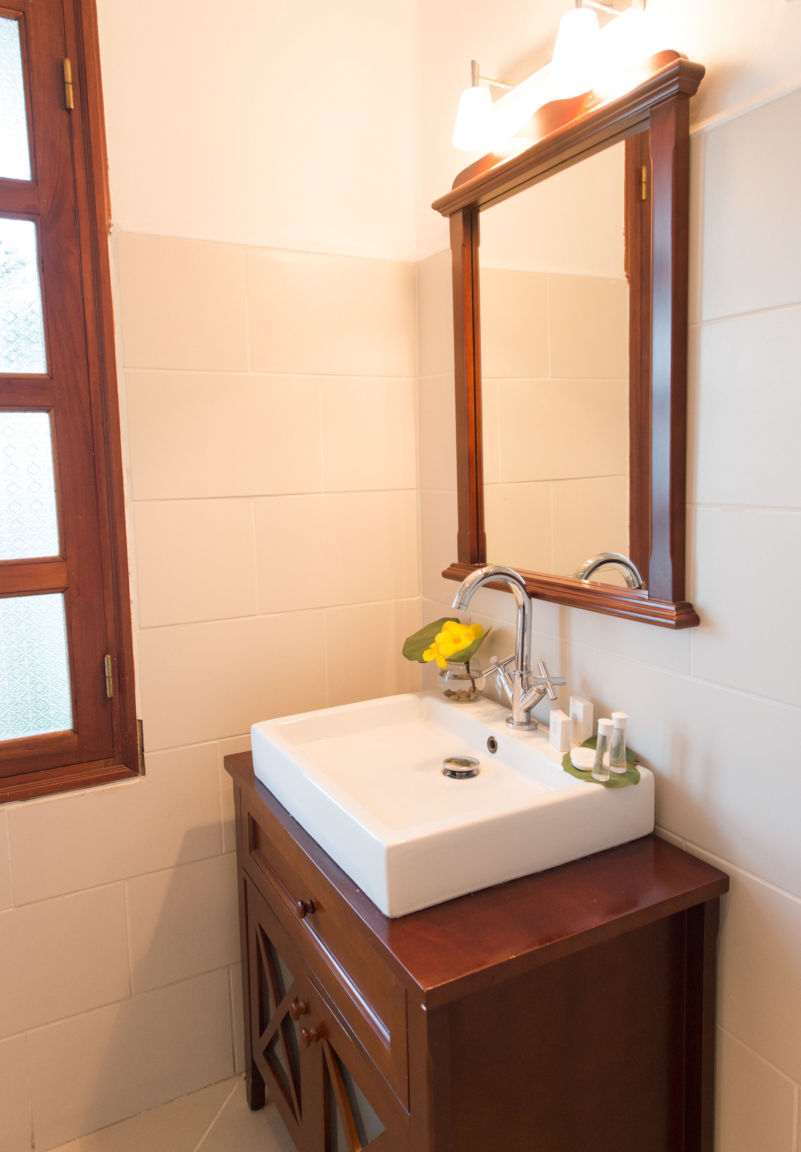 Un bagno con un lavandino bianco, un mobile contenitore in legno e uno specchio sopra il lavandino.