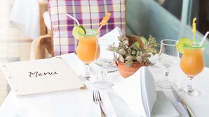 A restaurant setting with tables set for dining, featuring a menu, drinks, and a small potted plant. - Hotel L'Imperatrice (Fort-de-France)