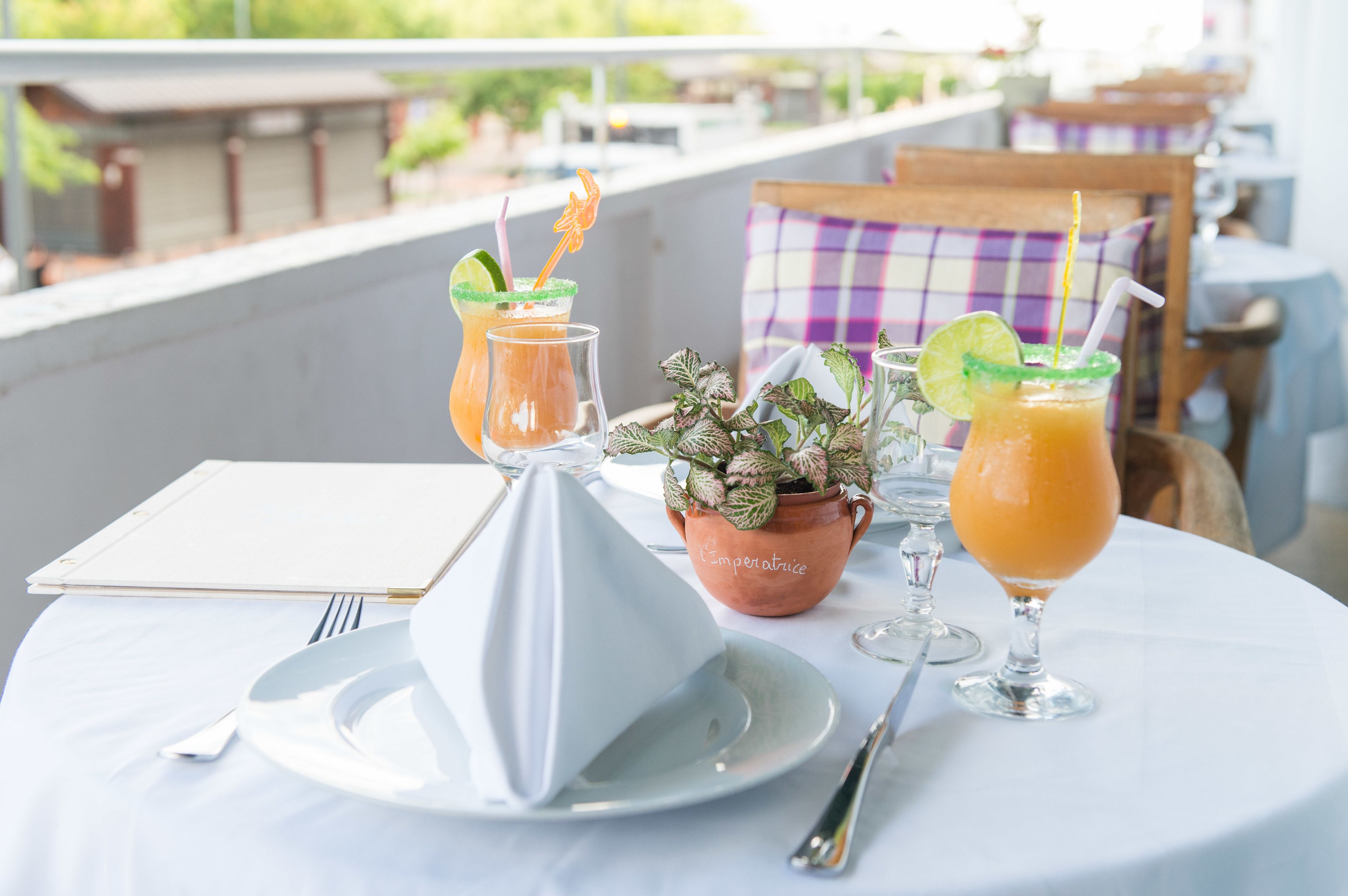 Una mesa con mantel blanco, dos bebidas adornadas con lima, una planta en maceta y un menú.