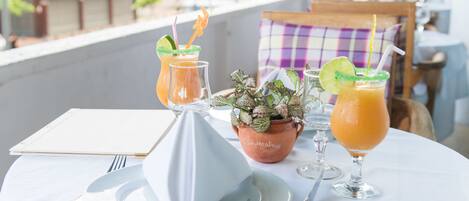 Una mesa con mantel blanco, dos bebidas adornadas con lima, una planta en maceta y un menú.