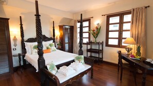 A four-poster bed with a wooden frame, a bedside table with a lamp, a chair, and a small table with fruit. - Hotel L'Imperatrice (Fort-de-France)