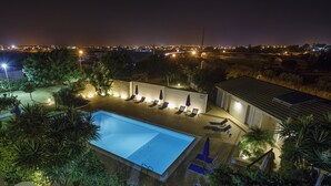 ’s Nachtzicht van een resort met een zwembad, ligbedden en een uitzicht op de stad in de verte.