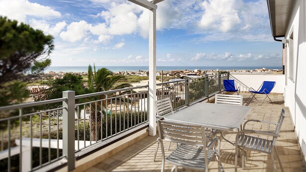 Een balkon met uitzicht op zee, een tafel en twee blauwe stoelen.