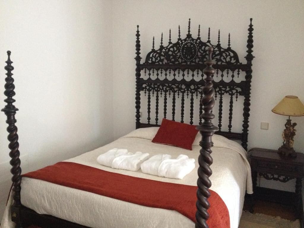 A neatly made bed with a red throw blanket, a white pillow, and a red accent pillow.