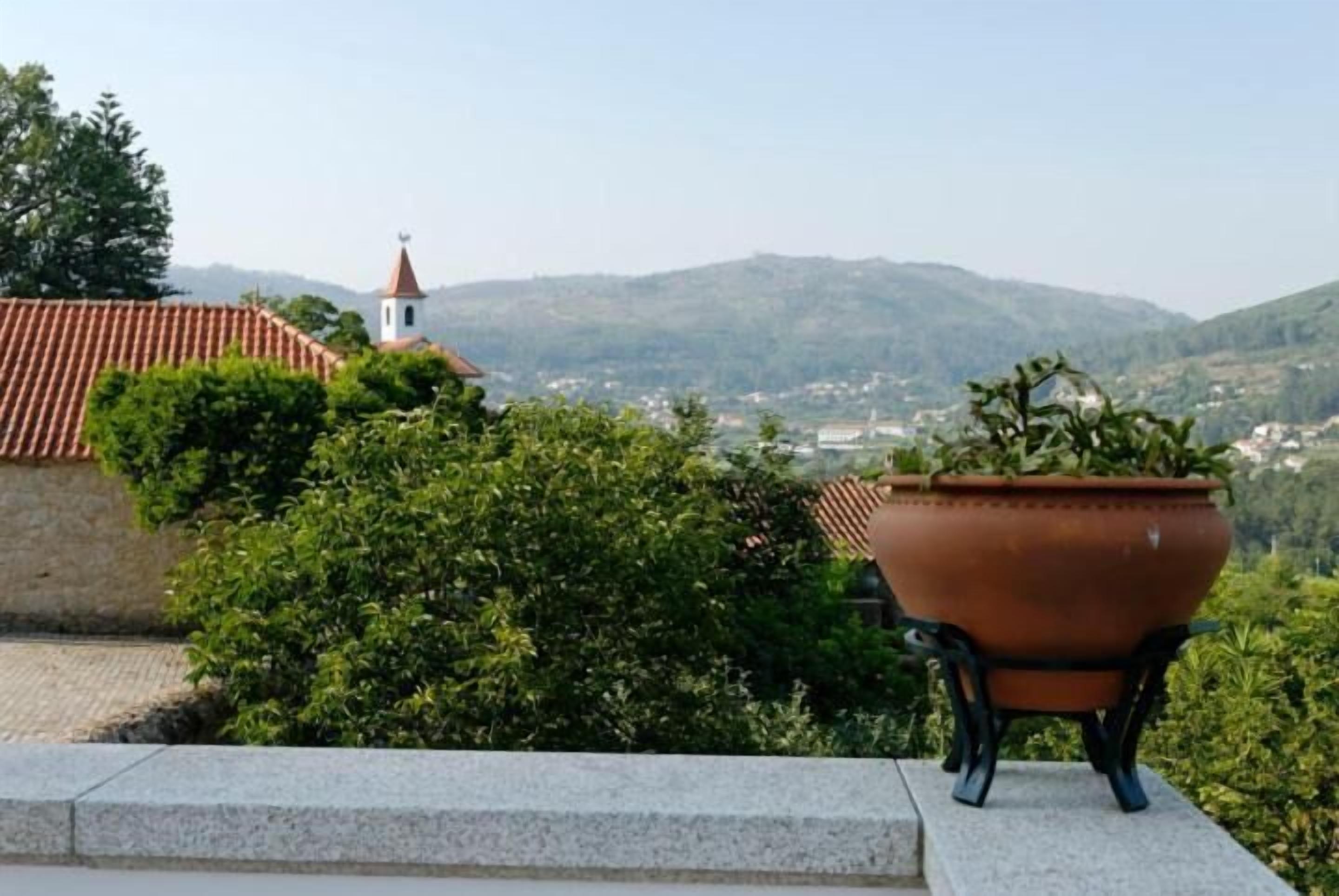 A terracotta pot on a balcony with a view of a church and hills.