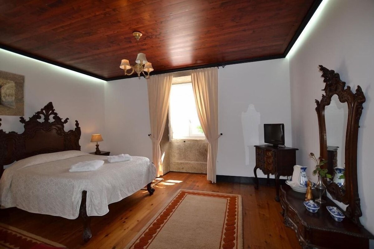 A bedroom with a wooden ceiling, a large bed with a white bedspread, a wooden dresser, a mirror, and a television on a side table.