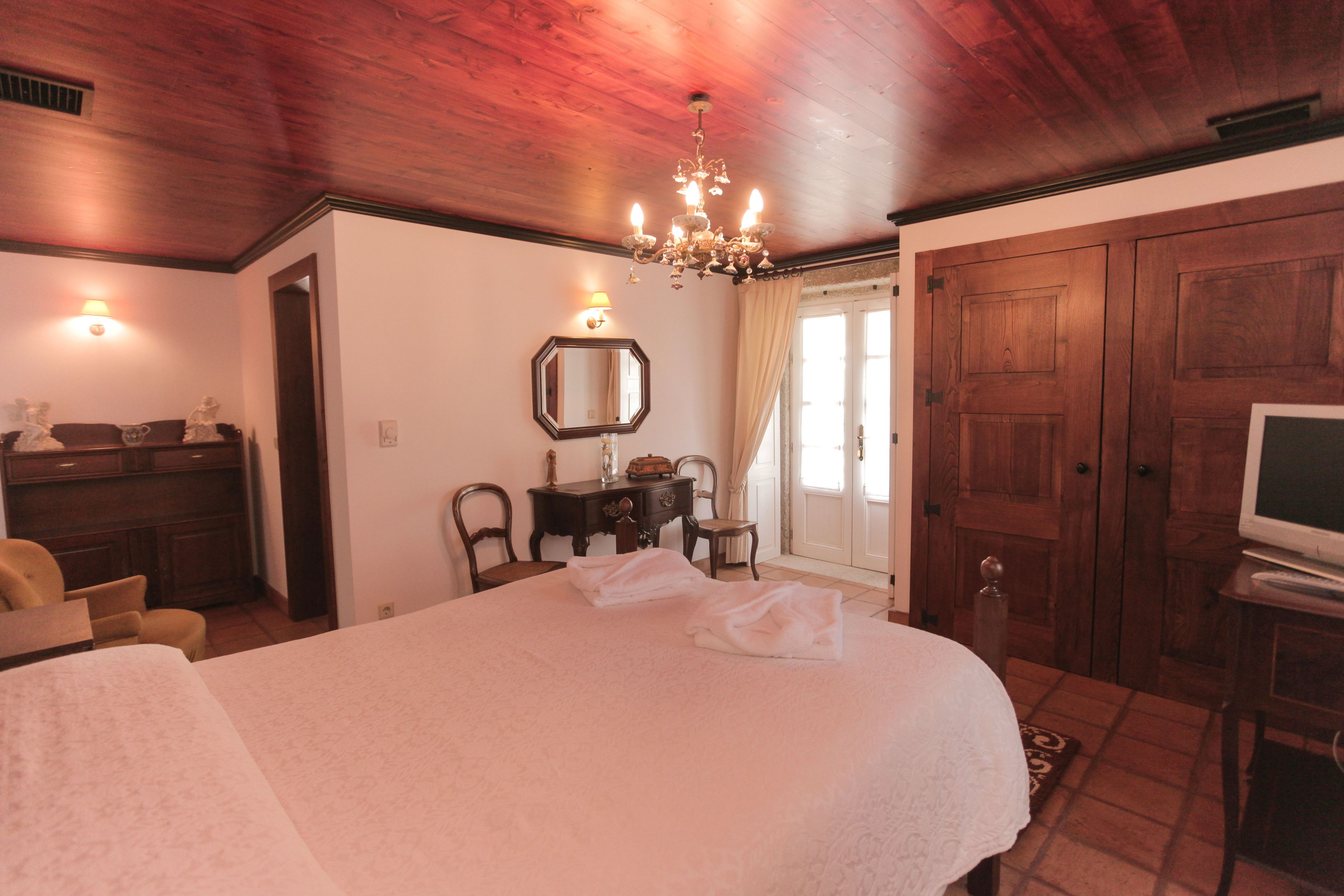 A bedroom with a large bed, wooden wardrobe, a desk with a mirror, and a television.