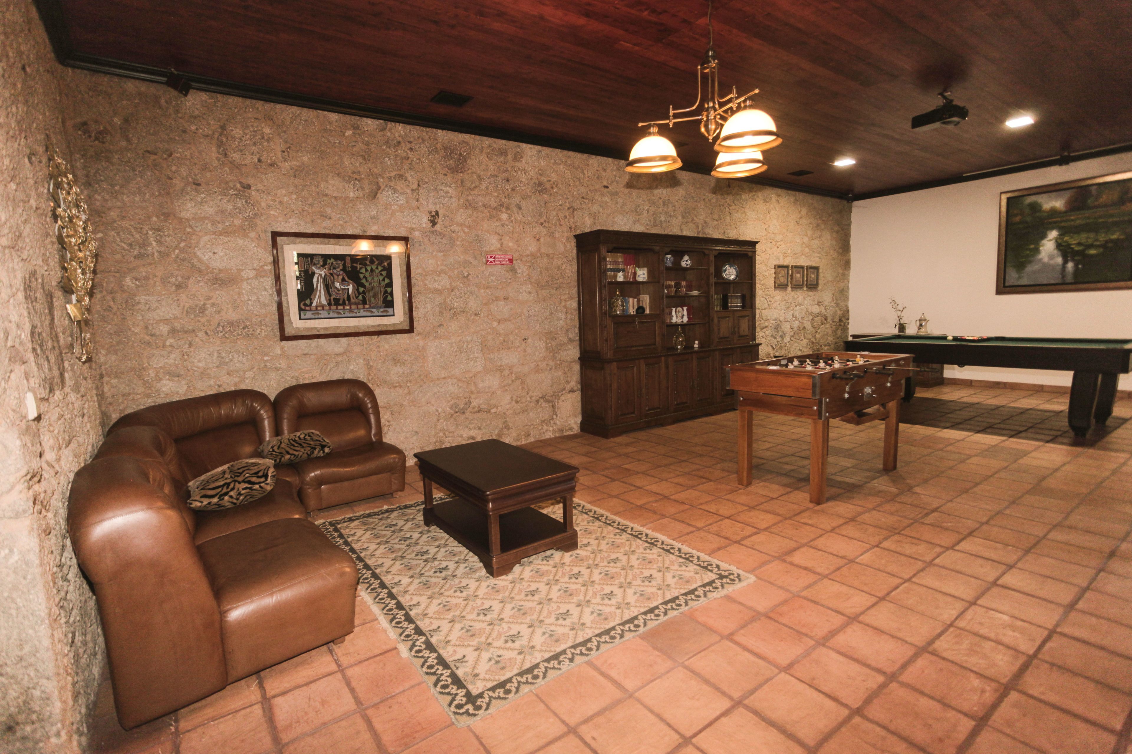 Um quarto com um sofá de couro marrom, uma pequena mesa de centro de madeira, uma mesa de bilhar e um armário com portas de vidro.