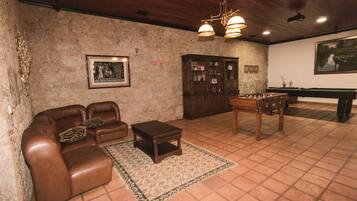 Um quarto com um sofá de couro marrom, uma pequena mesa de centro de madeira, uma mesa de bilhar e um armário com portas de vidro.