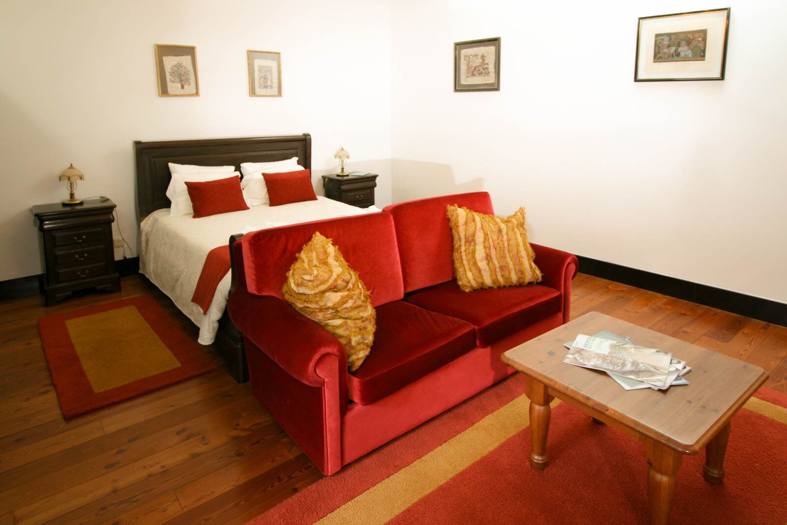 A hotel room with a bed, a red sofa, a wooden coffee table, and a small table with papers.