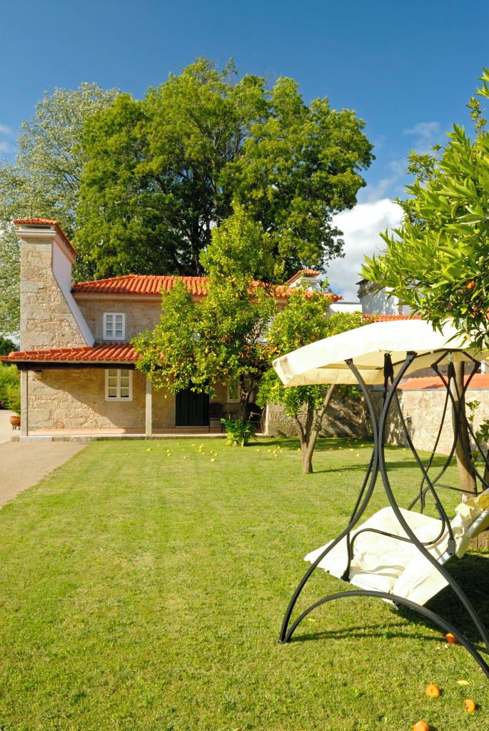 Une maison en pierre avec un toit en tuiles, une pelouse et une table en métal surmontée d’un parasol blanc.