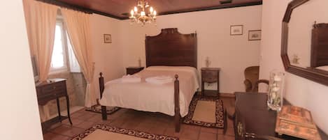A bedroom with a wooden ceiling, a large bed with a headboard, a chandelier, a dresser, and a mirror.