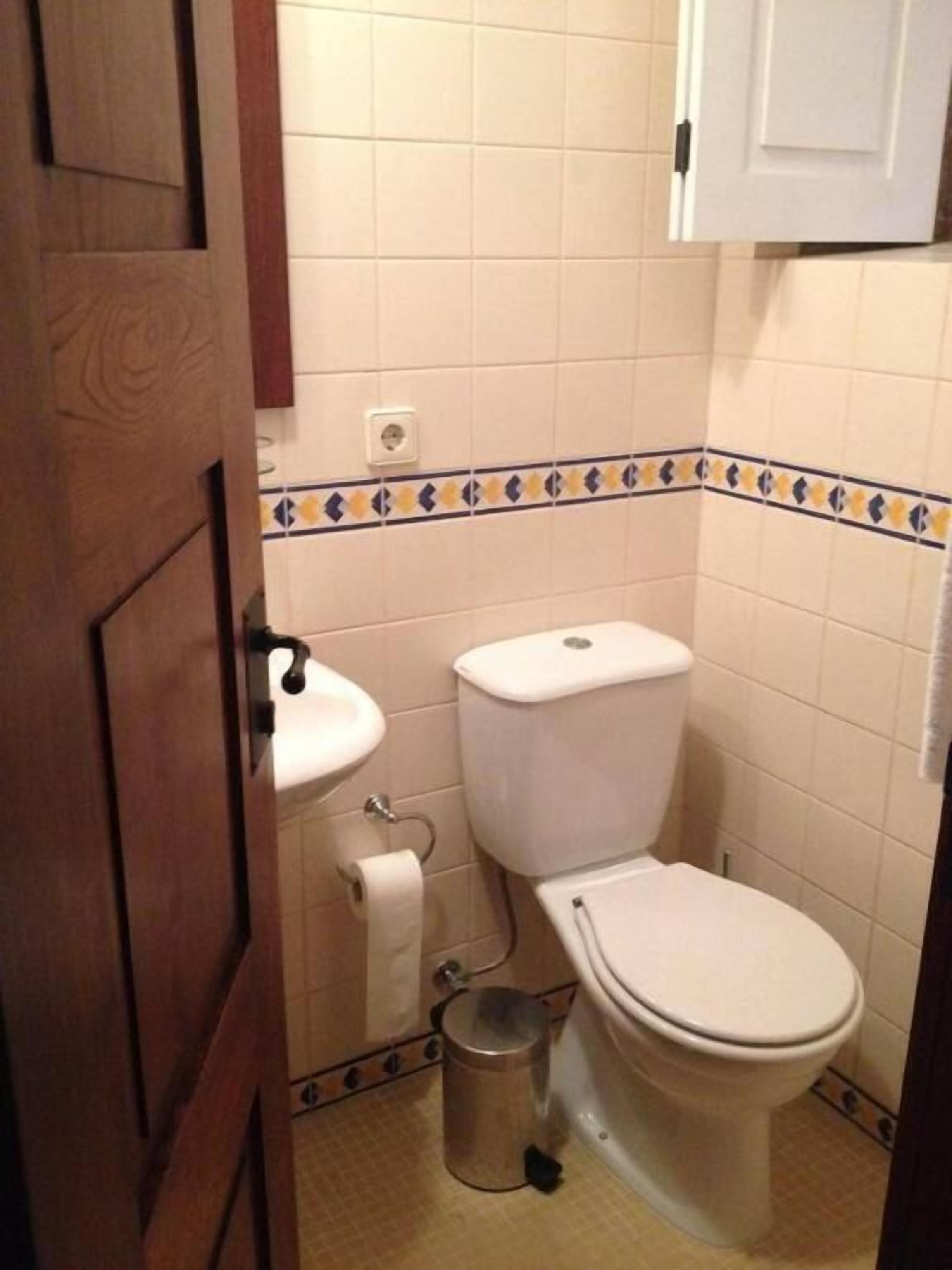 Un baño pequeño con inodoro, lavamanos y un cubo de basura.