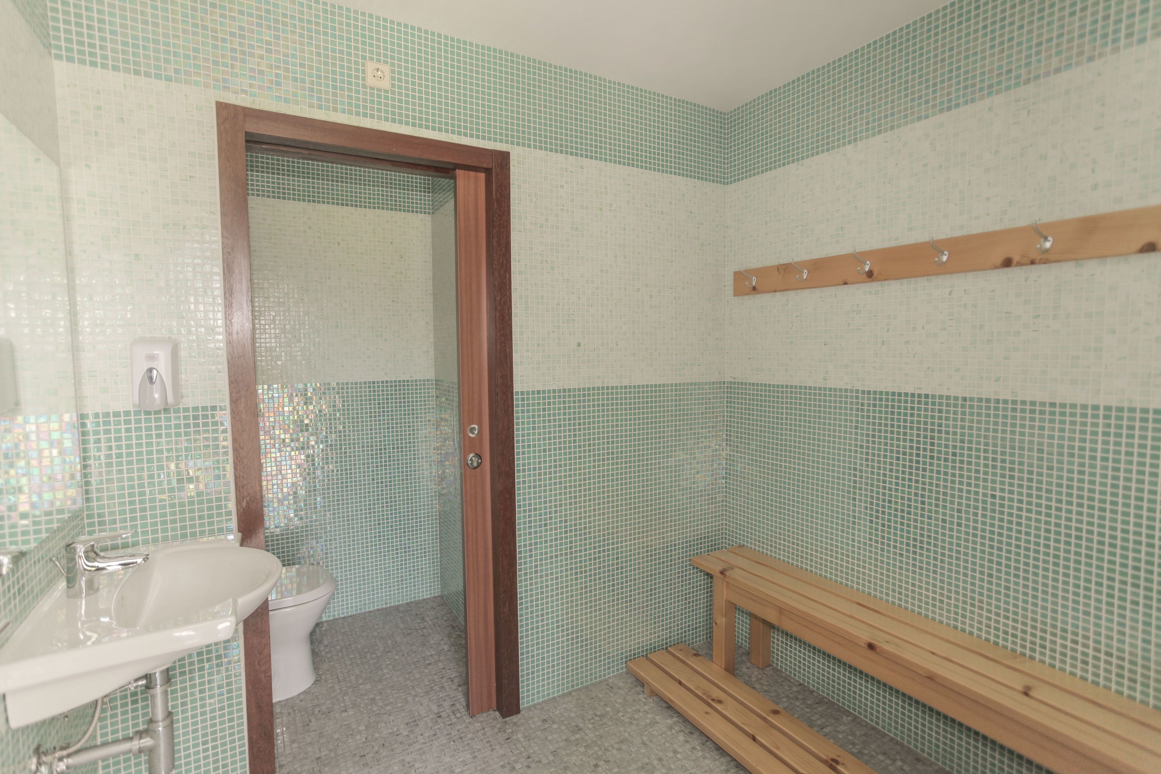 Un bagno con lavandino, wc e panchetta in legno.