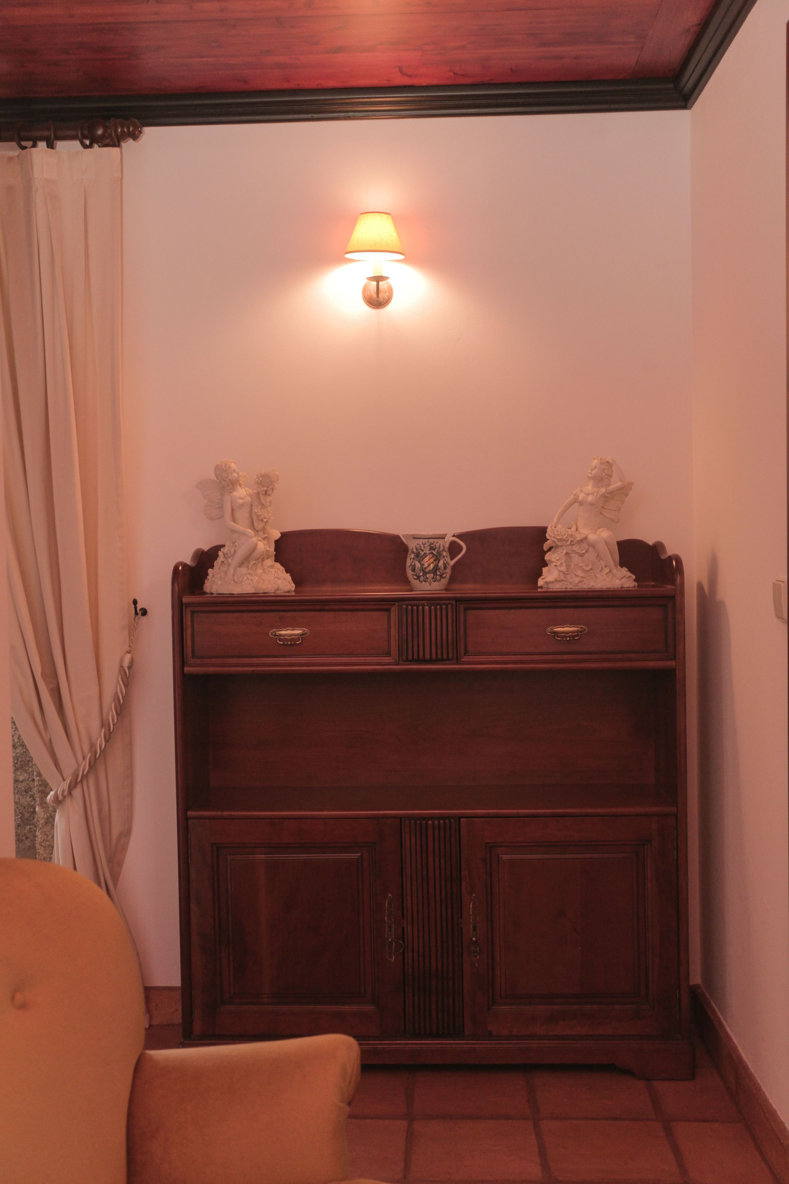 A wooden cabinet with two drawers and a shelf, a lamp above it, and a statue on the shelf.