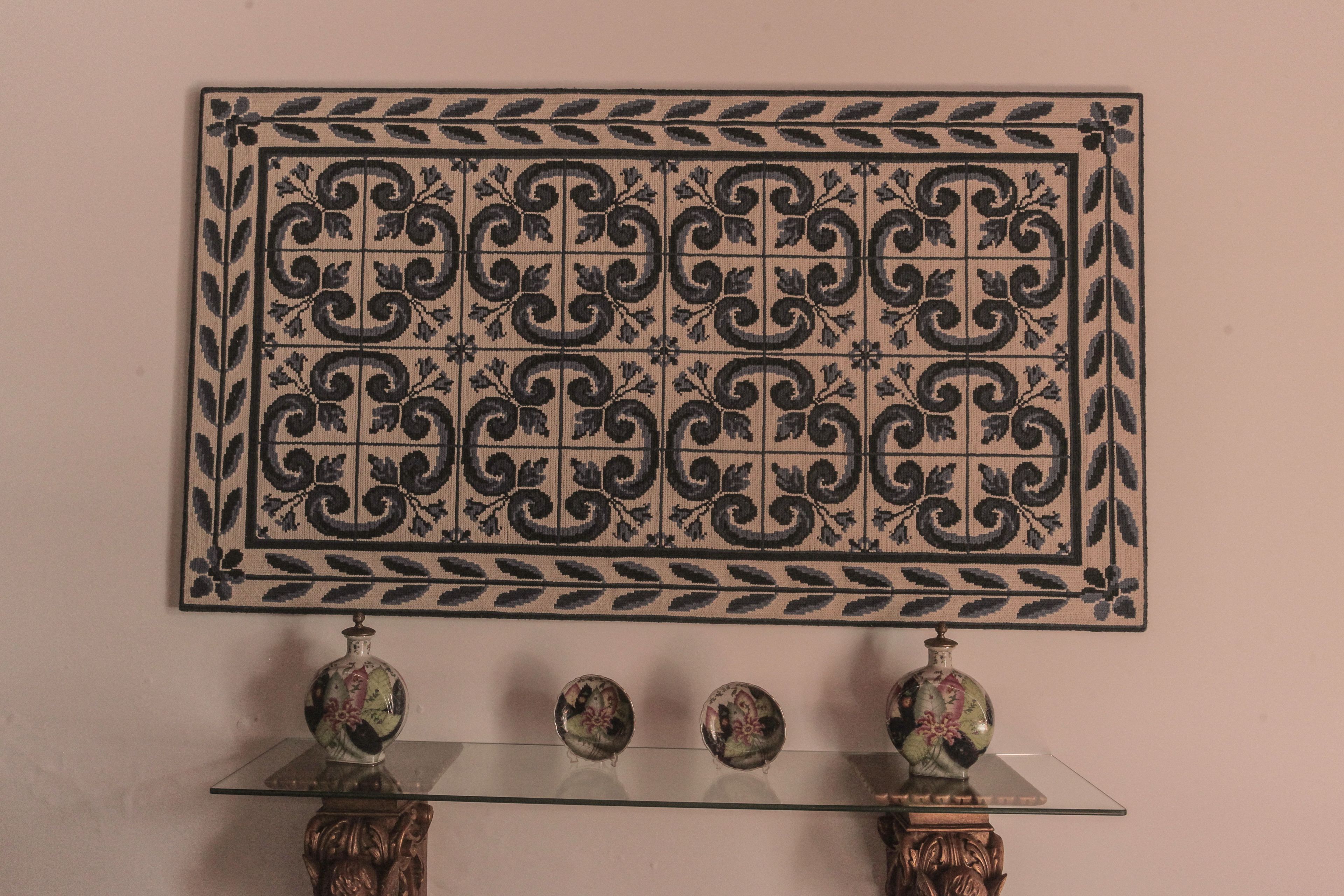 Una pared decorativa de azulejos con un diseño simétrico. Abajo, una mesa de cristal con dos jarrones ornamentales a cada lado.