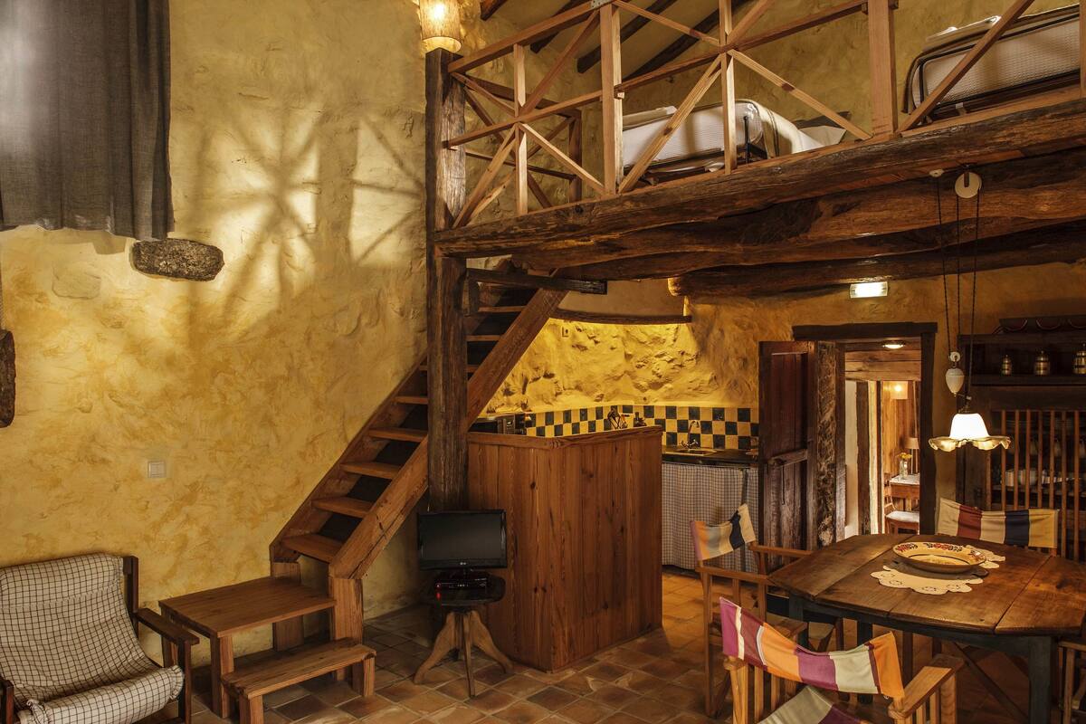 Een landelijke inrichting met een houten trap, een eethoek met tafel en stoelen, en een keuken in de achtergrond.