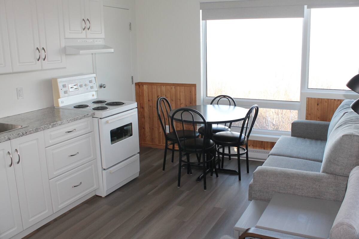 A compact kitchen with white cabinets, a stove, and a dining area with a table and chairs.