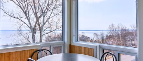 A room with a round table and four chairs, large windows with a view of a tree and a body of water.
