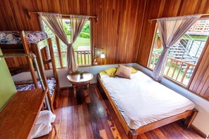 A wooden room with bunk beds, a single bed, a small table, and a window with curtains. - Pensión Santa Elena (Monteverde)