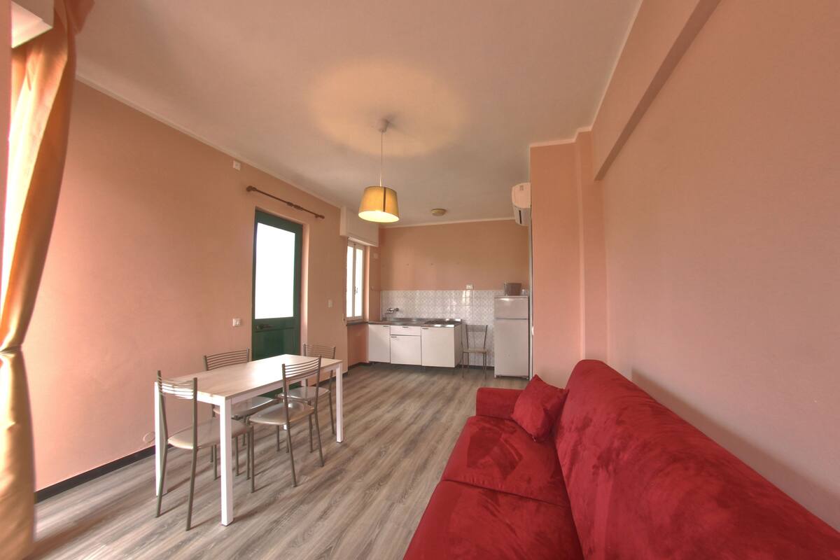 A compact living space with a dining area, kitchenette, and a red sofa.