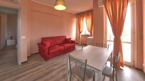 A room with a red sofa, a dining table with chairs, and a hanging light fixture. - Residence Riviera (Pietra Ligure)