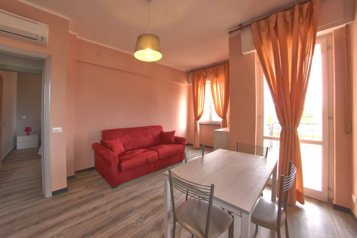 A room with a red sofa, a dining table with chairs, and a hanging light fixture.
