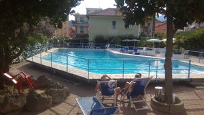 A swimming pool with a tiled deck, surrounded by lounge chairs and a railing. - Residence Riviera (Pietra Ligure)