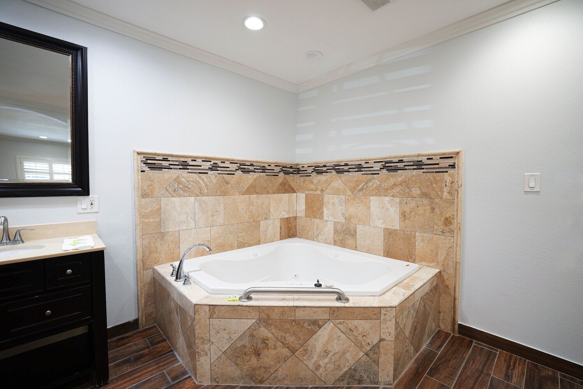 A bathroom with a large bathtub, a mirror, and a vanity with drawers.