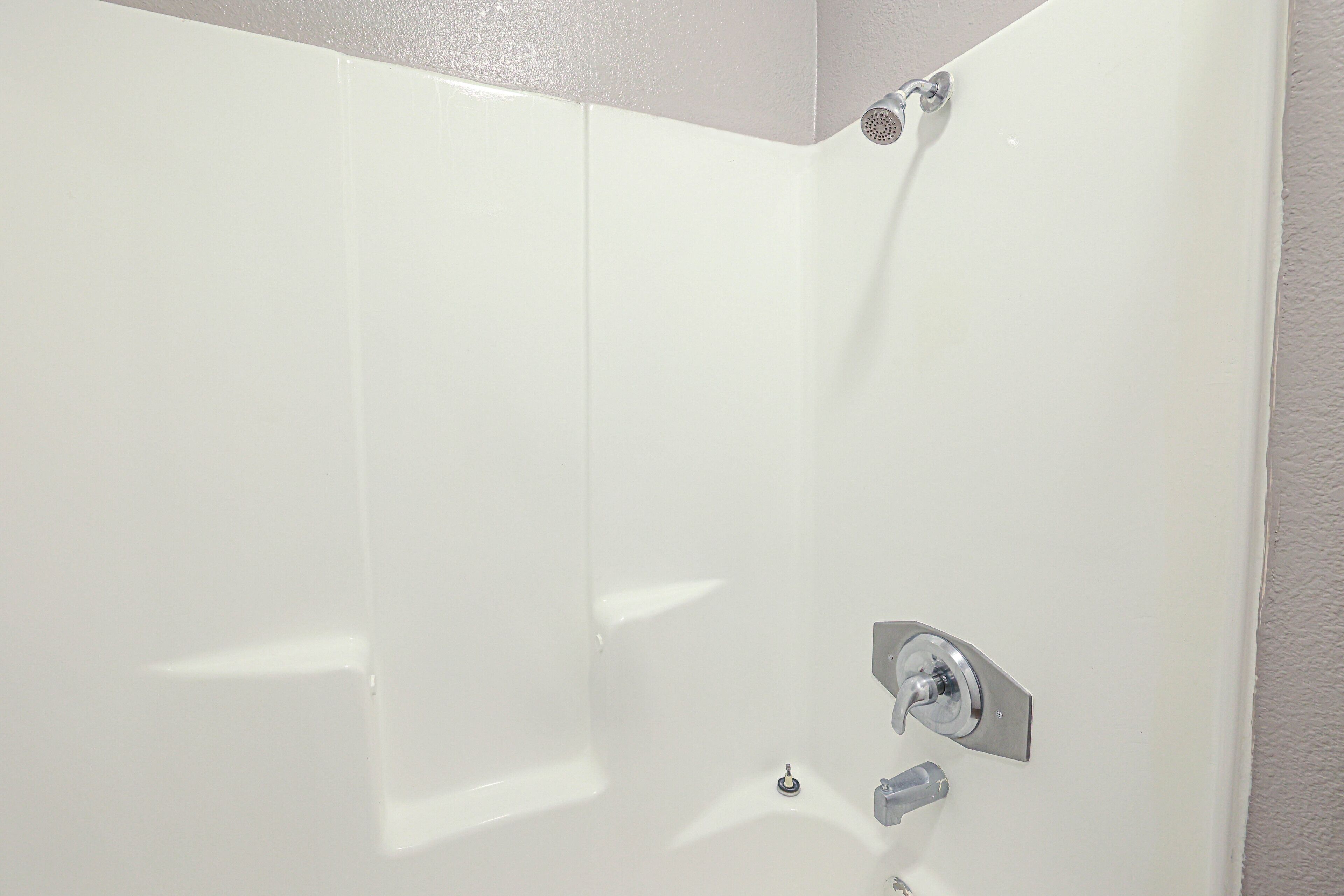 A white shower with a chrome faucet and a wall-mounted control.