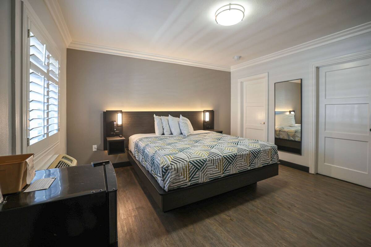 A bedroom with a bed, bedside tables, a dresser, a mirror, and a window with blinds.