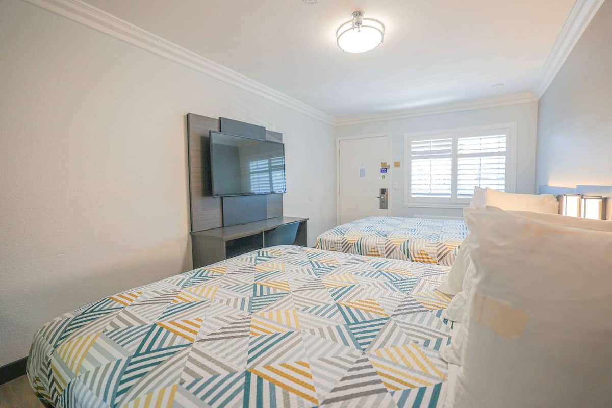 A bedroom with two beds, a TV, and a window with blinds.