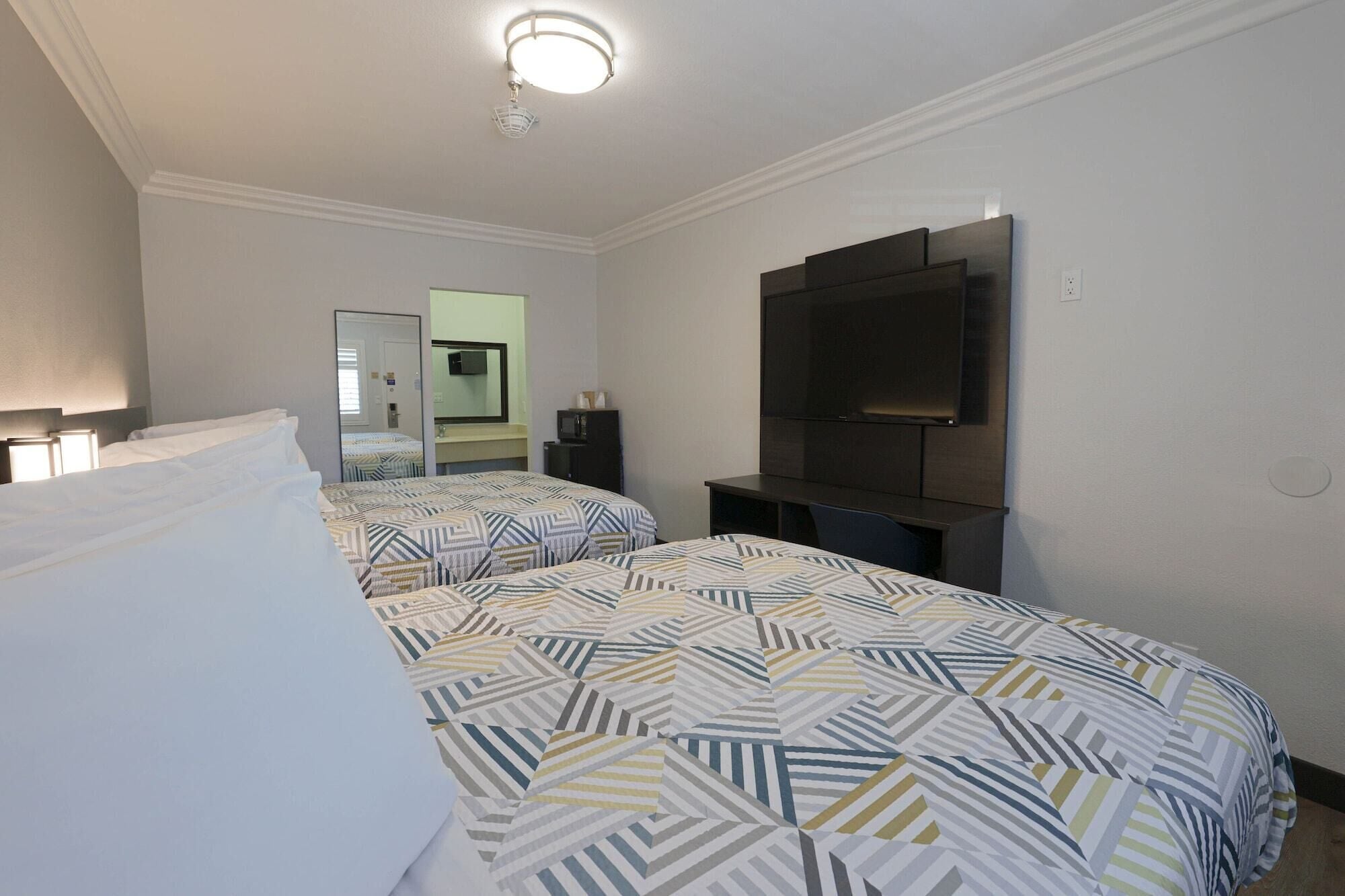 A hotel room with two beds, a TV, a mirror, and a ceiling light.