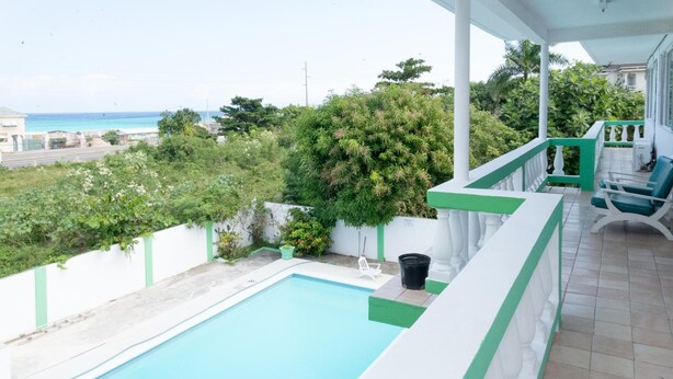 Piscina con vista al océano, rodeada de vegetación y una cerca blanca.