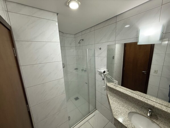 A modern bathroom with a glass-enclosed shower, a granite countertop, and a large mirror. - Paiaguás Palace Hotel (Cuiabá)