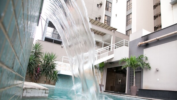 A pool with a waterfall feature, surrounded by a modern building with balconies and potted plants. - Paiaguás Palace Hotel (Cuiabá)