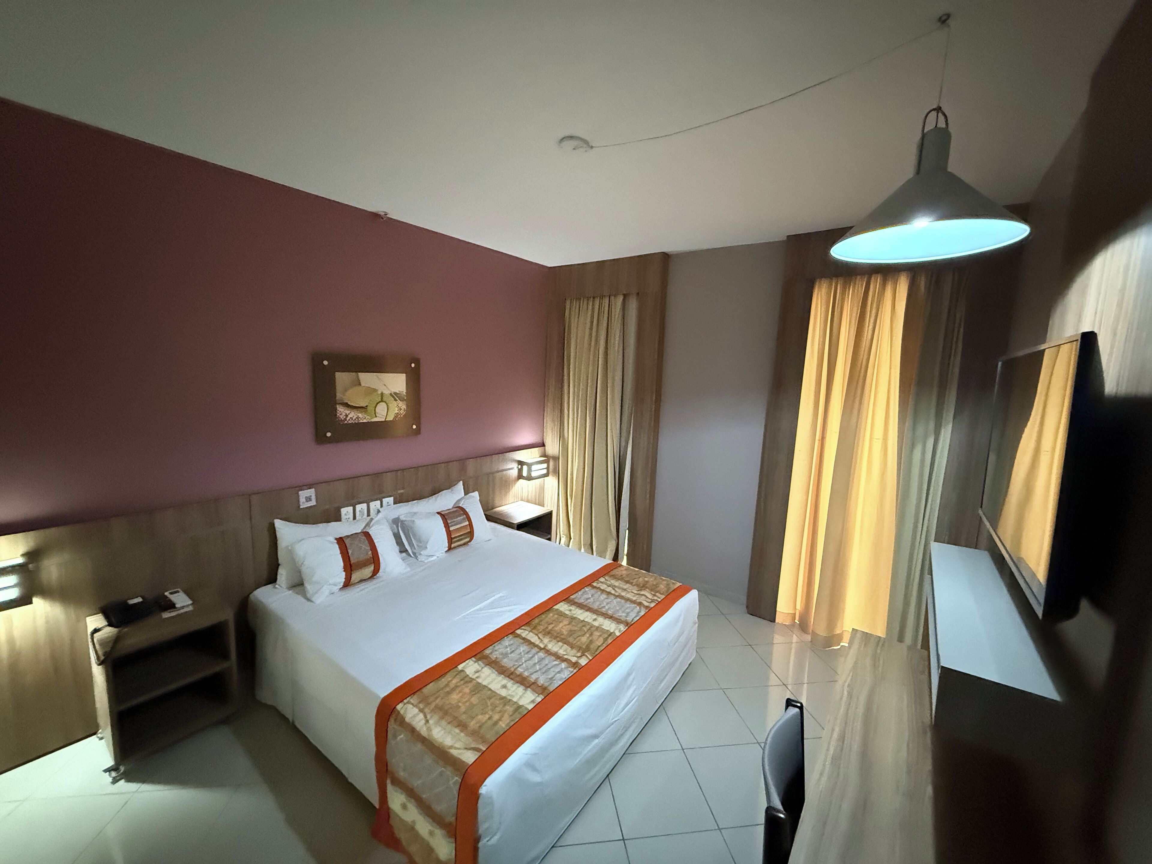 A hotel room with a bed, bedside tables, a desk, a chair, a TV, and curtains.