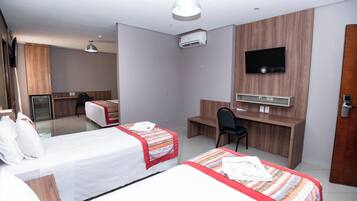 A hotel room with two beds, a desk, a chair, a TV, and an air conditioning unit.