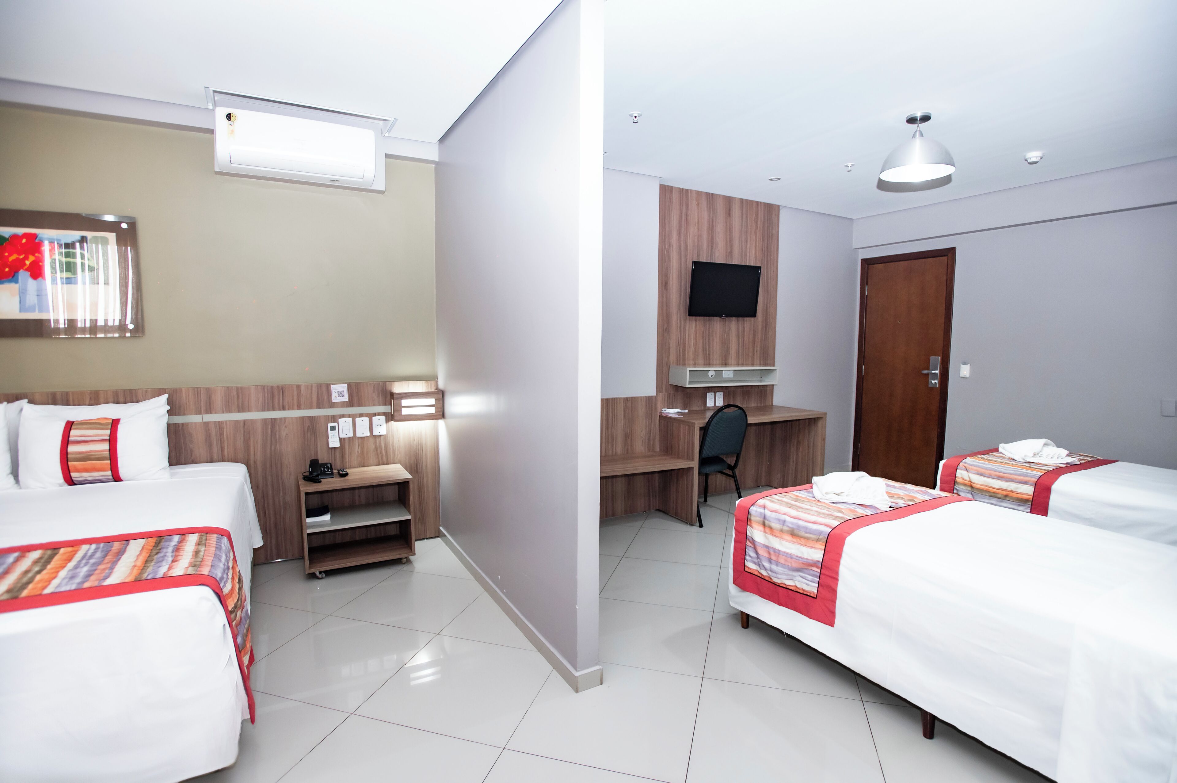 Quarto de hotel com duas camas, uma mesa, uma televisão e um guarda-roupa.