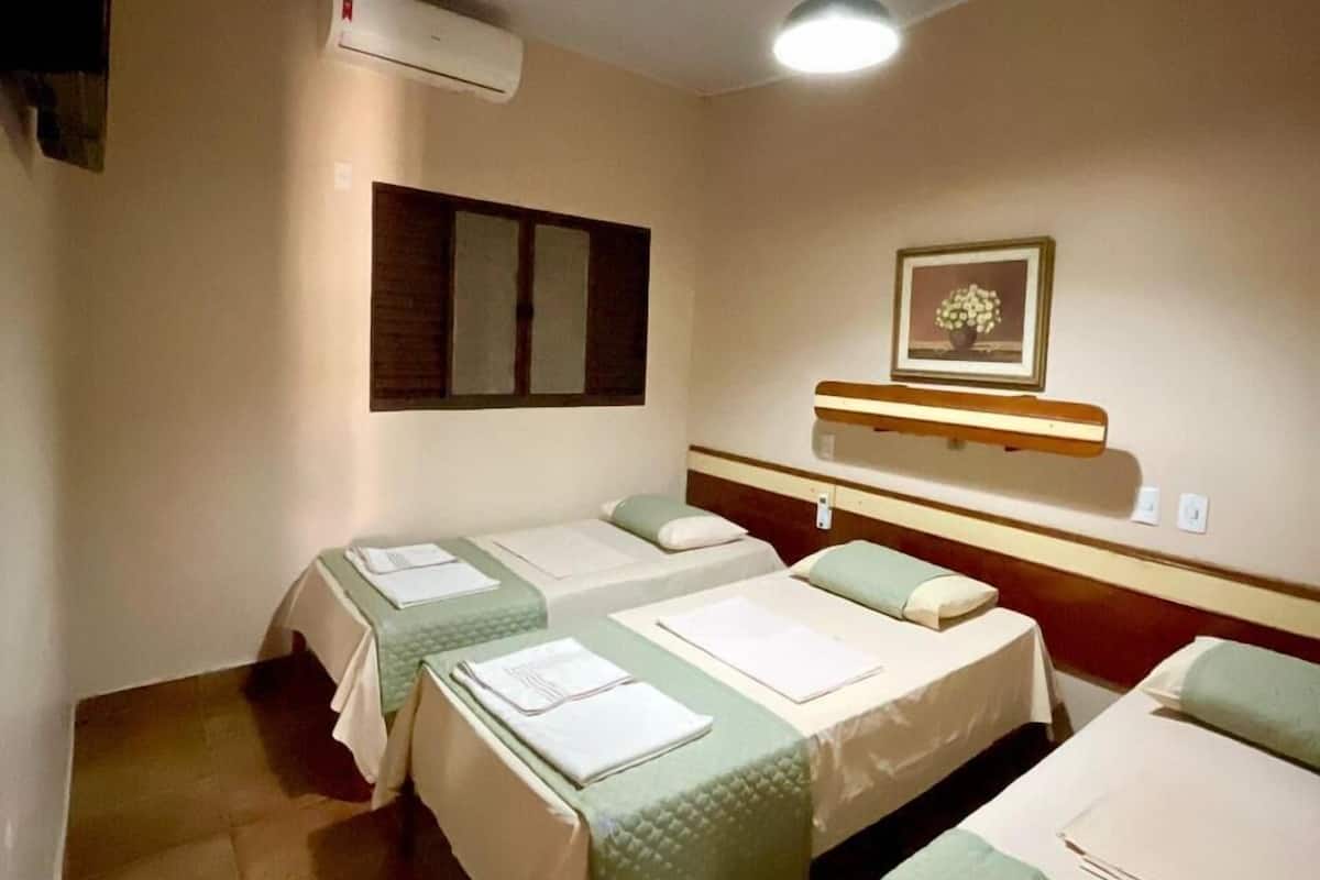 Ein Hotelzimmer mit zwei Einzelbetten, einem Nachttisch, einem Spiegel, einem an der Wand montierten Fernseher und einer Klimaanlage.