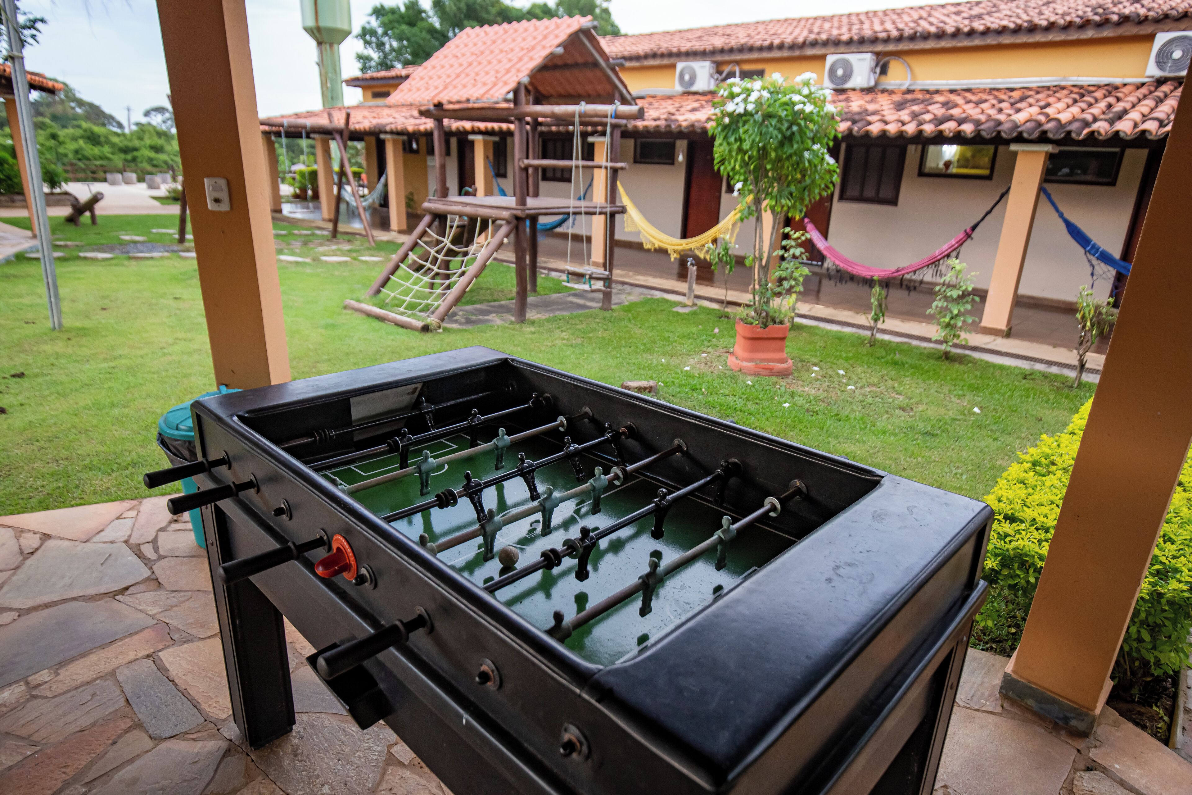 An outdoor Foosball table in a courtyard with a playground and a house in the background.