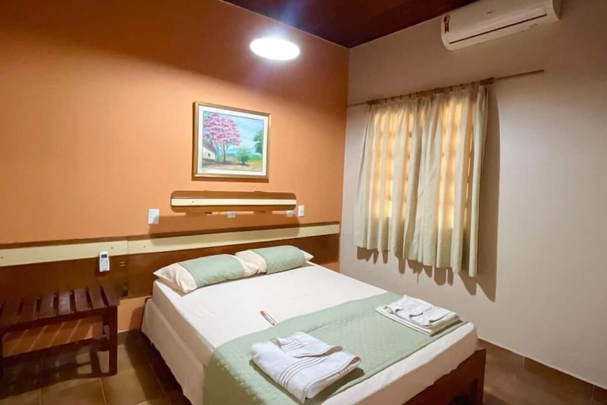 Ein Hotelzimmer mit Holzboden, einem Bett mit grüner Bettdecke, einer Bank und einem Gemälde an der Wand.