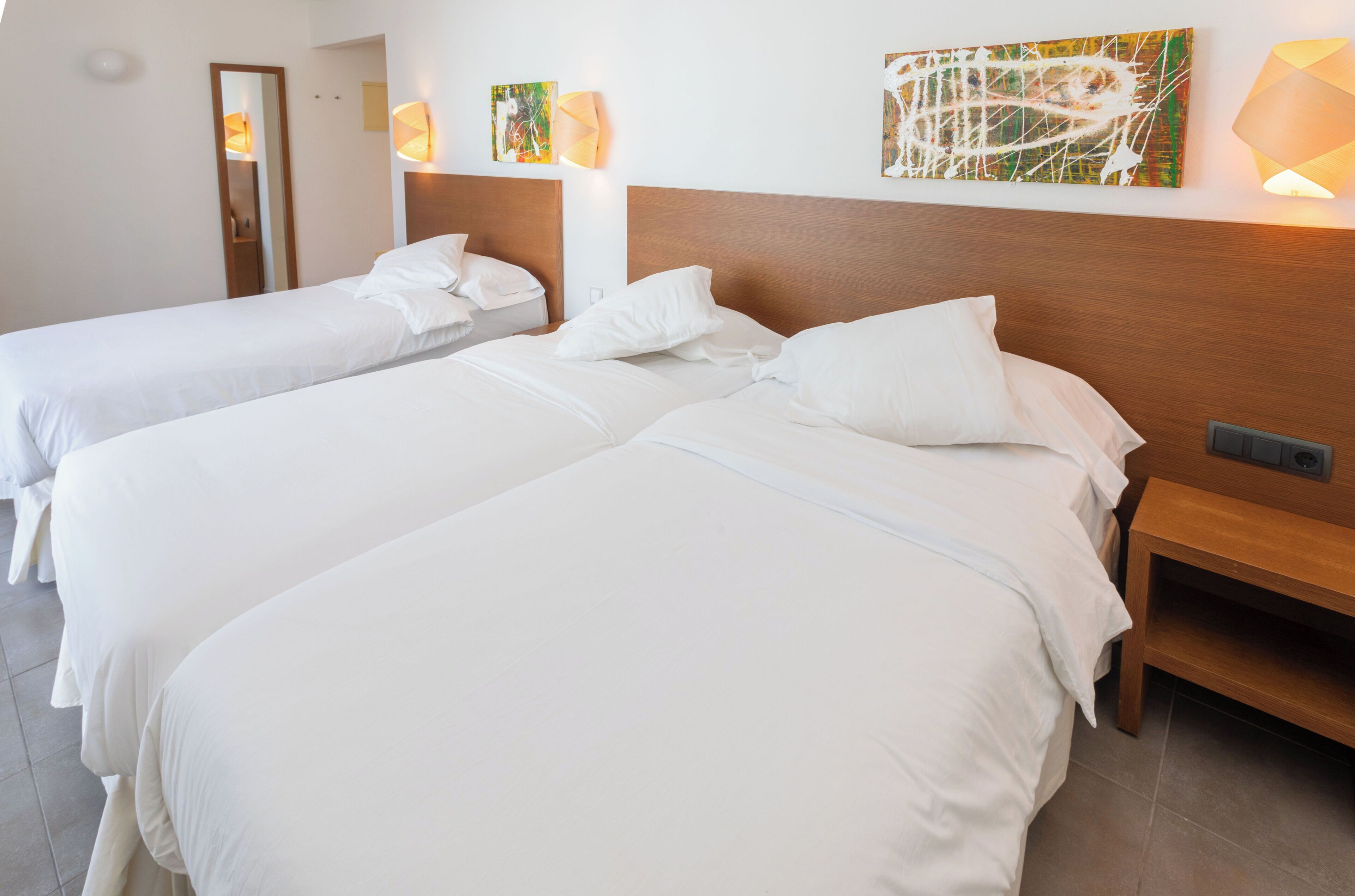 Une chambre d’hôtel avec deux lits, une tête de lit en bois, une table de chevet et des œuvres d’art accrochées au mur.