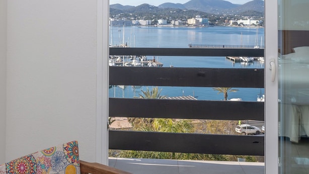 A balcony with a view of a marina and distant hills. - Hotel Es Mitjorn (Sant Antoni de Portmany)