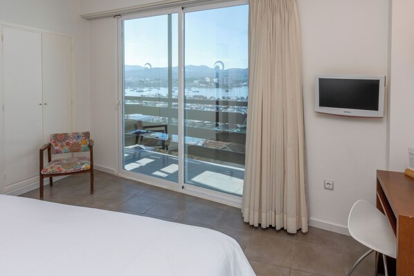 Habitación de hotel con cama, televisor montado en la pared, una silla y balcón con vistas a la ciudad.