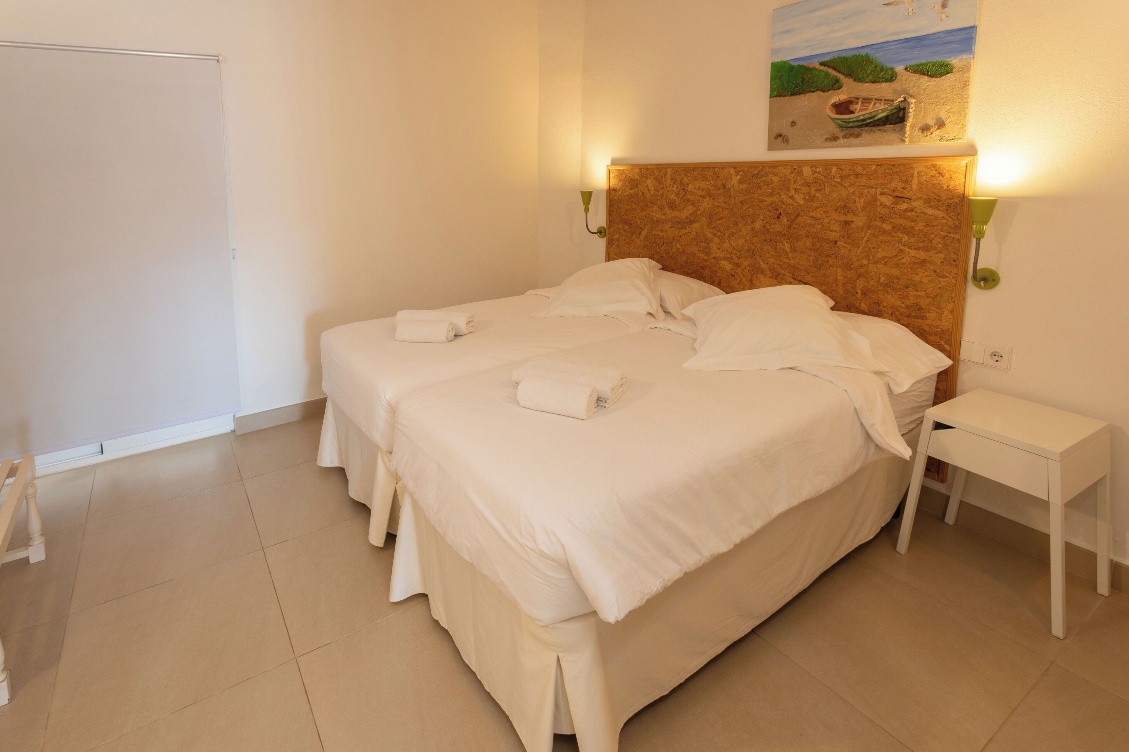 A hotel room with a large bed, two bedside tables, a headboard, a painting on the wall, and a whiteboard.